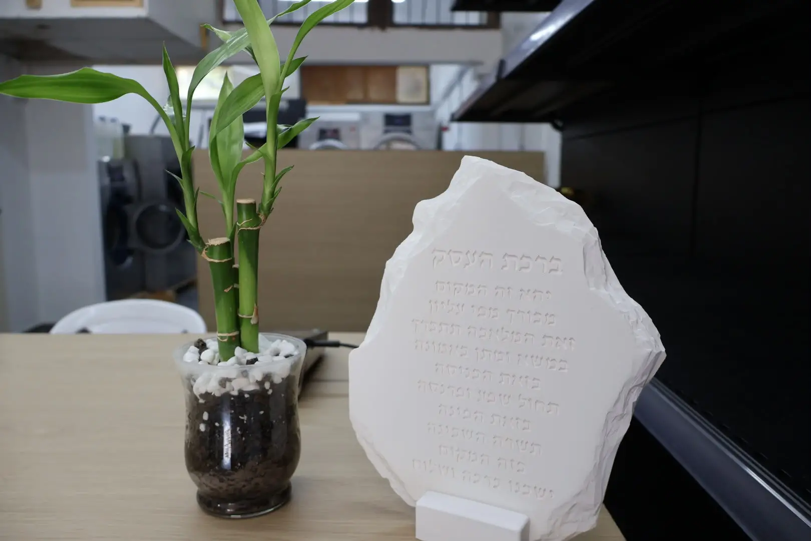 פינת הדלפק במכבסה עם לוח ברכת העסק וברקע חדר העבודה והמכונות התעשייתיות
